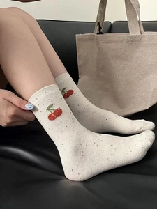 Detail of cream rib-knit mid-calf sock with red cherry embroidery and colorful flecks