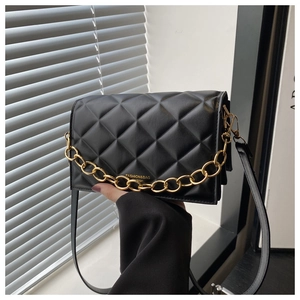 Close-up of black quilted shoulder bag featuring gold chain strap and leather handle