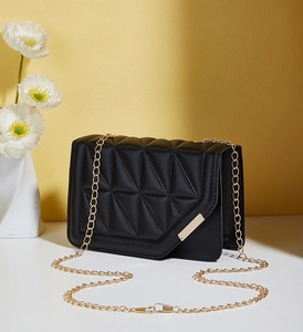 Detail of black crossbody bag with geometric triangle quilting and gold bar fastener