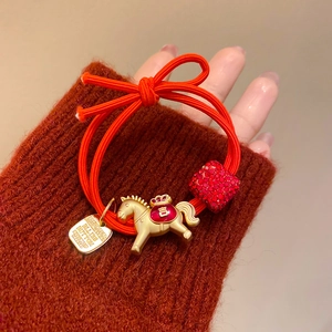 Détail d'un élastique à cheveux rouge avec pendentif cheval doré et perle rouge