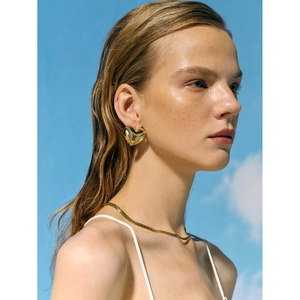 Close-up of elegant 18k gold heart earrings with crystals on a model against the blue sky
