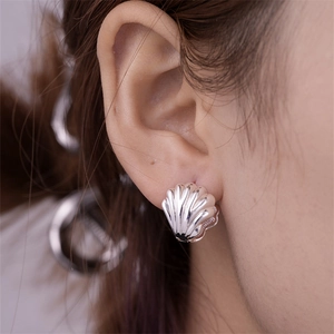 Macro shot of silver shell-shaped earrings on model ear showing polished texture
