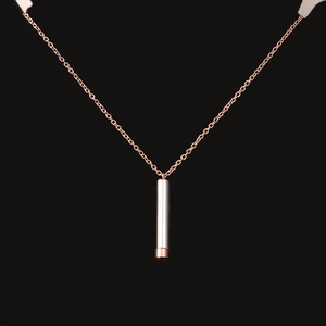 Detailed macro view of a silver and rose gold cylindrical pendant necklace on a dark base