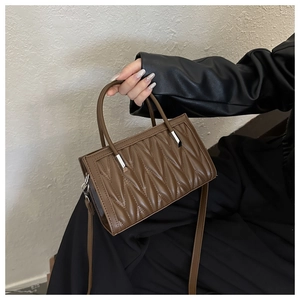Detailed view of brown quilted bag with silver hardware and adjustable strap on a shoulder