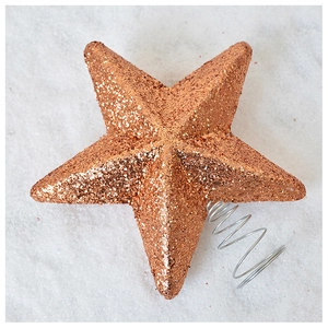 Close-up of rose gold Christmas tree topper star with metallic glitter and spring base