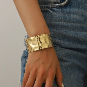 Wide gold-tone open cuff bracelet with hammered metal texture on female model's wrist