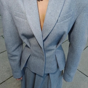 Détail de la veste cintrée bleu-gris et de la jupe plissée en tissu style laineux