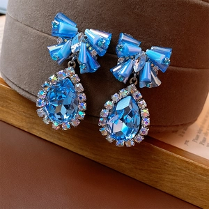 Close-up of blue crystal bow water drop earrings on a premium velvet jewelry stand