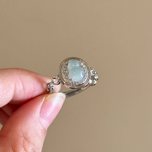 Close-up of a green jade gourd ring with silver wavy band and sparkling accents