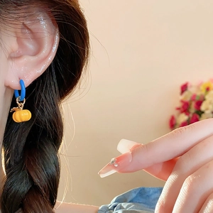 Detail of blue circular earring with orange pumpkin pendant worn by a model