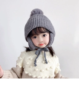 Detailed knit texture of children's grey winter earflap hat with soft pom-pom detail