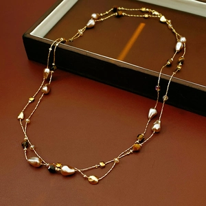 Dettaglio di collana a strati con perle occhio di tigre e perle barocche su pelle scura