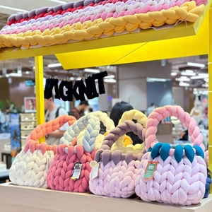 Handmade chunky knit bag in vibrant candy colors displayed on a yellow retail shelf