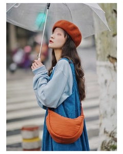 Close-up of orange nylon crescent crossbody bag styled with casual outdoor outfit