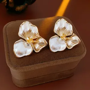 Elegant white floral stud earrings with gold trim on a brown velvet jewelry box
