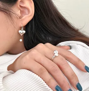 Close-up of minimalist 925 sterling silver knotted ring and 3D heart earrings set on model