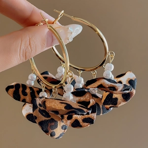 Detail of leopard print fabric fringe and white pearls on golden hoop earrings