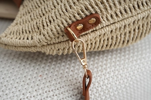 Detailed macro view of woven beach bag with brown leather trim and gold metal buckle