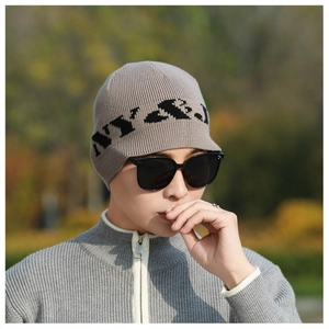 Detail of grey knitted beanie with NY jacquard pattern worn by male model outdoors