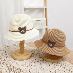 Detailed view of woven straw hats featuring a cute bear crochet patch and brown ribbon