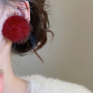 Gros plan sur des boucles d'oreilles pompon rouge duveteux portées par un mannequin