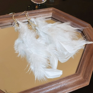 Close-up of bohemian white feather earrings with gold chains on a mirrored tray