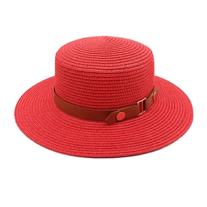 Detailed macro view of red straw boater hat with brown faux leather band and metal buckle