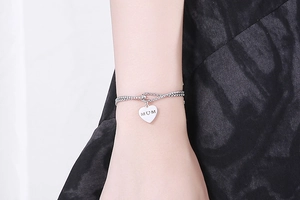Detailed view of silver heart pendant with MOM engraving on a layered box chain bracelet