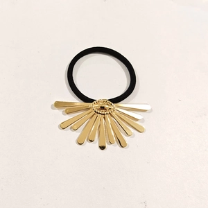 Detail of a golden seven-petal floral metal charm on a black elastic hair tie