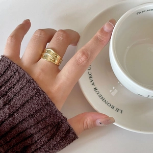 Detail of a wide gold wavy ring with unique liquid texture on a hand with a white cup