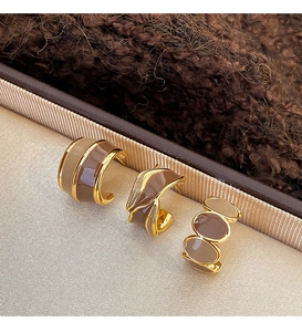 Detailed macro view of vintage gold and brown enamel hoop earrings on beige silk fabric