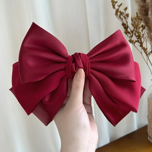 Macro detail of luxury burgundy satin bow hair clip with elegant layered silk texture