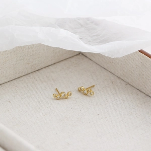 Close-up of golden s925 silver bubble stud earrings with cubic zirconia on linen box