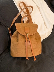 Detailed view of brown faux suede backpack featuring drawstrings and polished leather trim