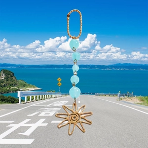 Detail of a golden sun pendant with blue crystal beads hanging over a coastal road scene