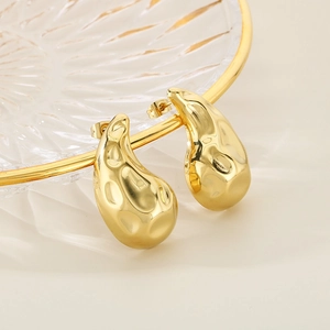 Detailed close-up of golden teardrop earrings with hammered texture on a glass tray