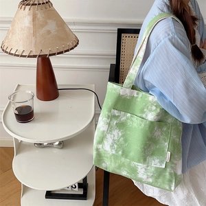 Dettaglio della borsa tote in tela tie-dye verde con tasca frontale in ambiente casual