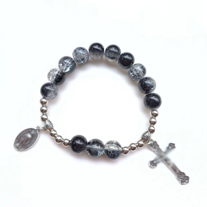 Dettaglio del bracciale con perle di vetro nere e un ciondolo a forma di croce in argento