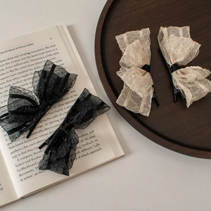 Elegant lace bow hair clips in black and beige displayed on a book and wooden tray