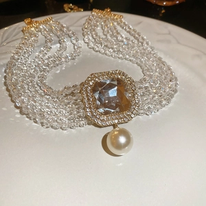 Detailed view of multilayer crystal choker with square gemstone and pearl drop on white ceramic