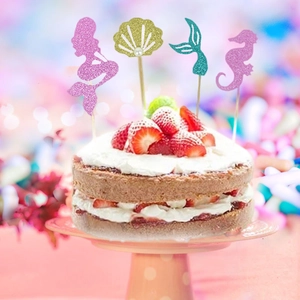 Glittery mermaid and seashell cake toppers on a strawberry dessert for party decor