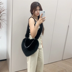 Close-up of heart-shaped black plush crossbody bag with metallic chain on a model