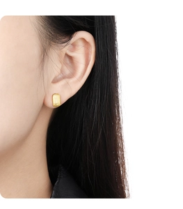 Close-up of golden geometric square stud earring with brushed texture on female ear