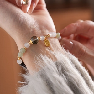 Detail of beaded bracelet with green crystals and golden blessing charm on wrist