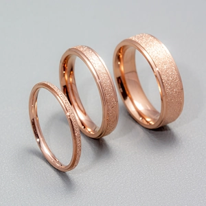 Three rose gold 2mm frosted stainless steel rings with glitter texture on gray background