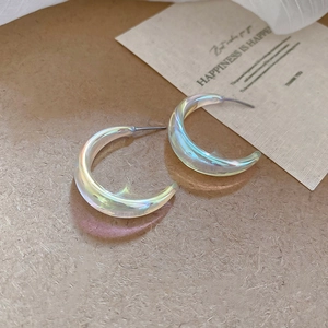 Macro view of C-shaped acrylic earrings with iridescent finish on textured paper
