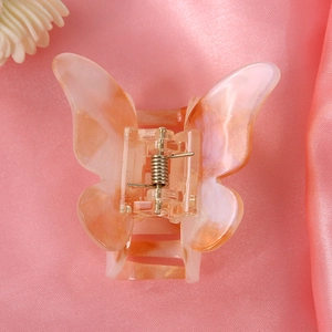 Close-up of butterfly hair claw clip in orange pink marble finish on pink silk fabric