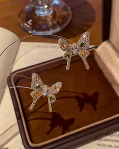 Macro shot of silver bow earrings with olive green and amber stones and micro-pave crystals