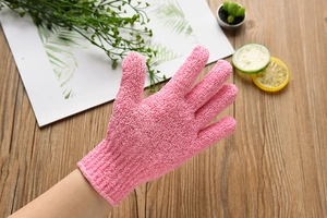 Detail of pink exfoliating bath glove with five-finger design on a wooden desk