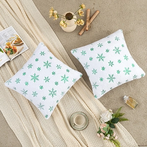 Cozy home setting with white plush pillow covers featuring green embroidered snowflakes
